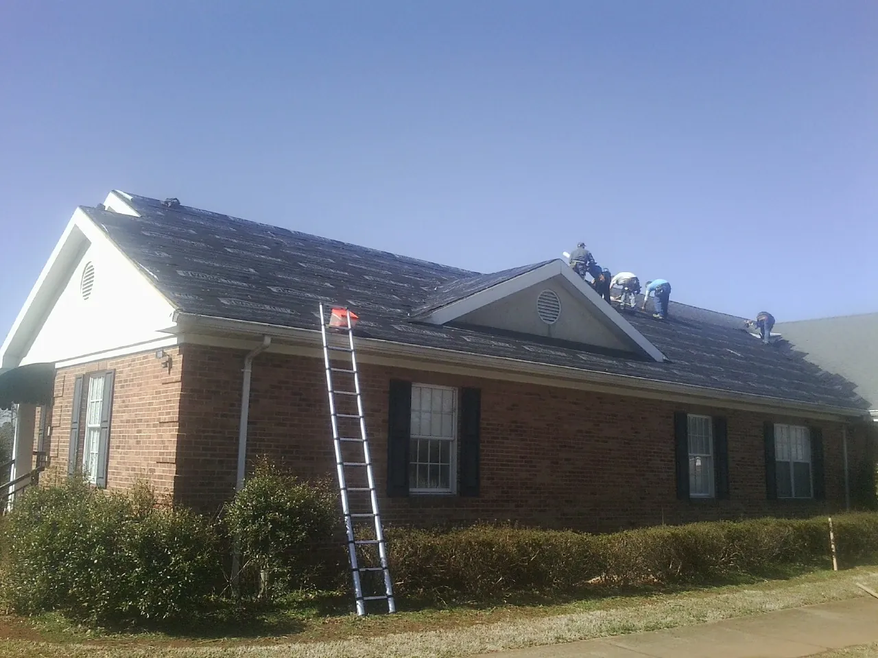 Crew tearing shingles off a brick ranch roof with a ladder set — Emergency Roof Repair work by our crew in Tilton