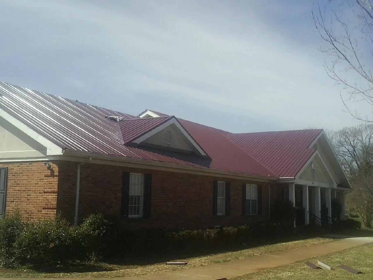 Red metal roof with gabled entries on a long brick building, from a Hail Damage Roof Repair job in Tilton