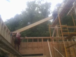 Carpenter raising a rafter beam on a new second story frame in Tilton