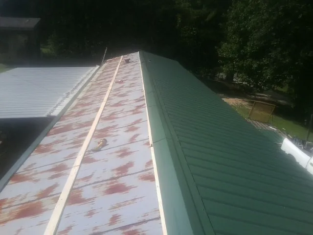 Old rusted panels beside newly installed green metal roofing — Wind Damage Roof Repair by Roofing Brothers in Tilton