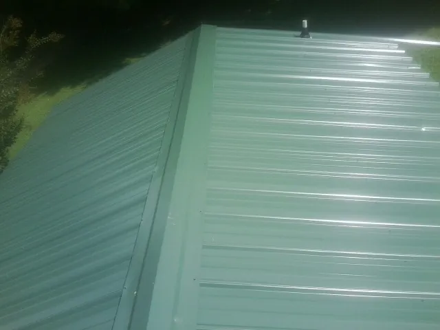 New green metal panels meeting at the ridge of a roof — Flat Roof Repair work by our crew in Tilton