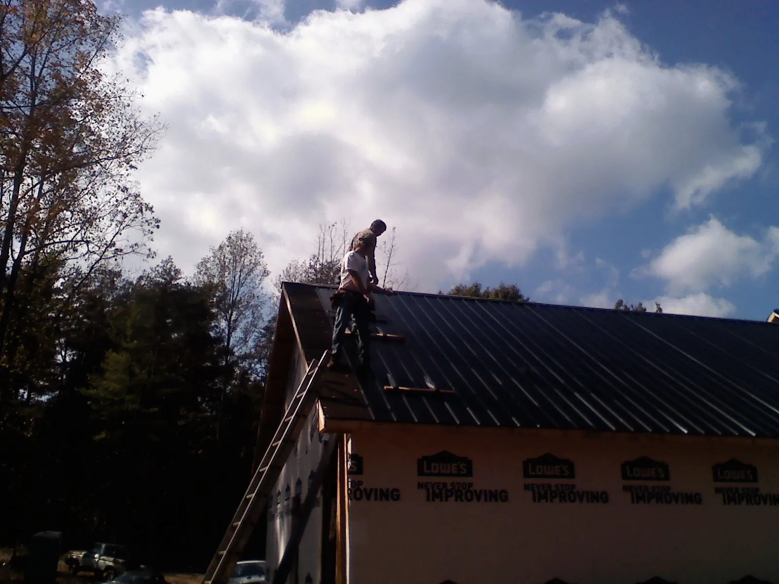 Roofer fastening dark metal panels high against a cloudy sky, from a Roof Inspection job in Tilton